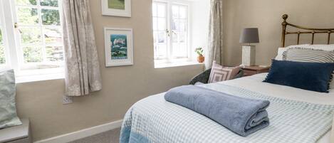 A bedroom with a bed, a nightstand, a lamp, and two windows with curtains.