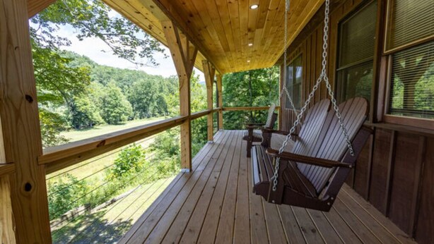 Eine Holzterrasse mit Schaukelstuhl, Geländer und Blick auf eine bewaldete Landschaft.