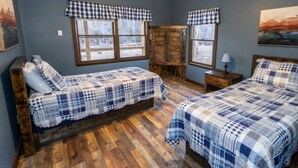Ein Zimmer mit zwei Betten, Holzboden, Deckenventilator und einem Fenster mit kariertem Vorhang.