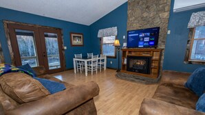 A living room with a stone fireplace, a television, and a dining area with chairs and a table. - Twin Falls Cabin Top Duplex (Spruce Pine)