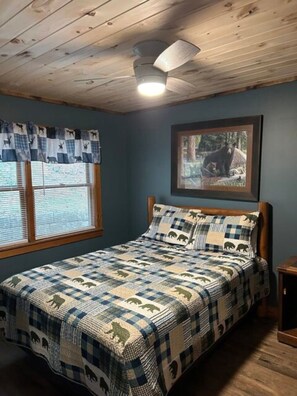A bedroom with a bed, a ceiling fan, a window with blinds, and a framed picture on the wall. - The River View Cabin (Spruce Pine)