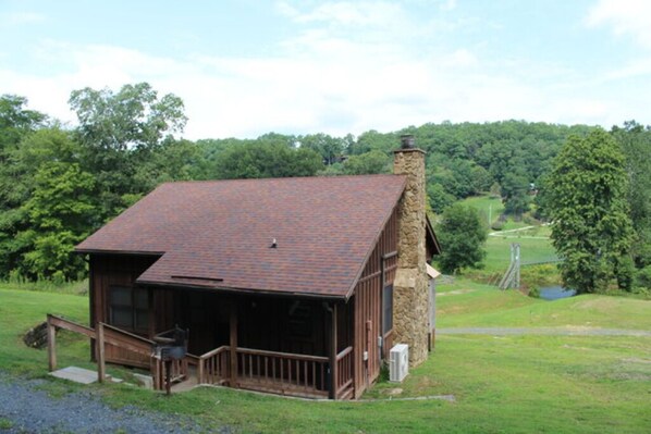 A rustic cabin with a stone chimney, a porch, and a view of a green landscape. - The River View Cabin (Spruce Pine)