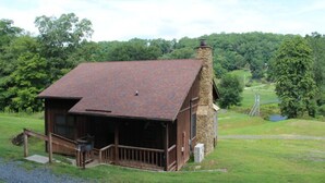 A rustic cabin with a stone chimney, a porch, and a view of a green landscape. - The River View Cabin (Spruce Pine)