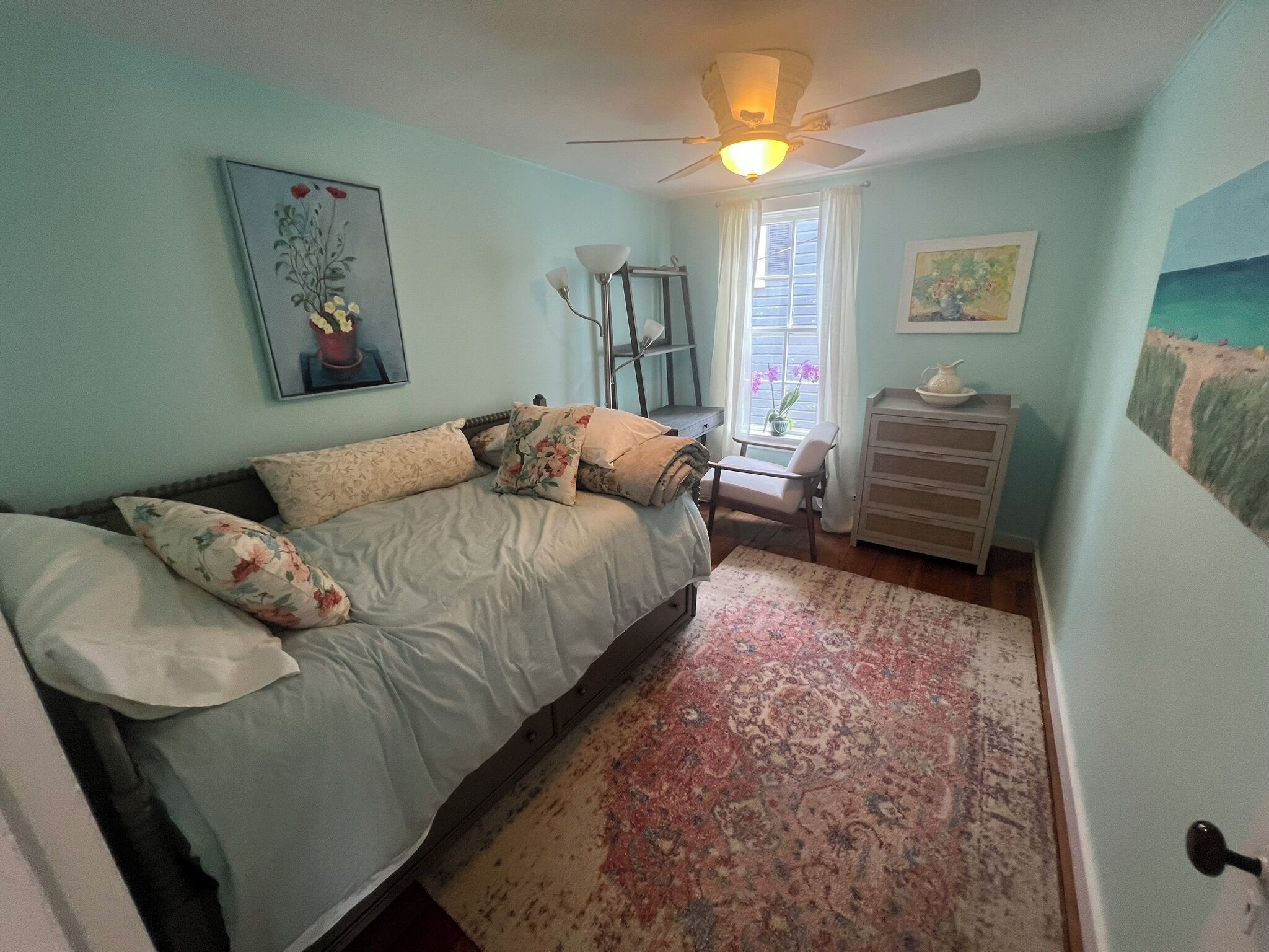 A bedroom with a bed, a nightstand, a dresser, a ceiling fan, and a window with curtains.