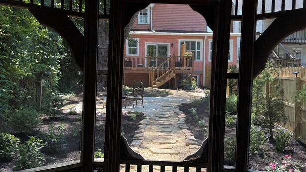 Ein hölzernes Gartenhaus mit Blick auf ein rosa Haus und einen Garten.