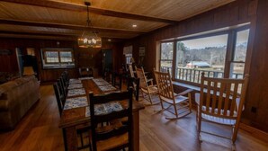 A wooden interior with a dining table and chairs, a sofa, and a view through large windows. - The Valley Lodge Sleeps 12 (Spruce Pine)