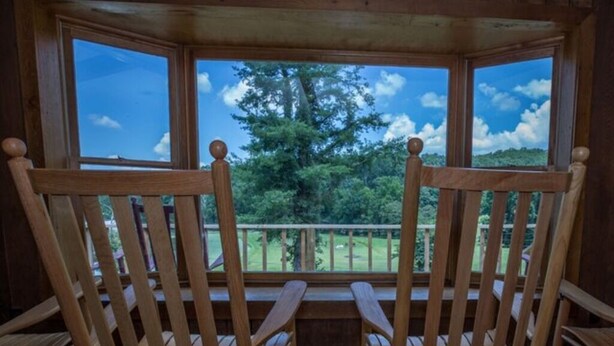 Two wooden rocking chairs facing a wooden deck with a view of a green landscape and trees. - The Valley Lodge Sleeps 12 (Spruce Pine)
