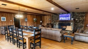 A cozy living room with a stone fireplace, wooden ceiling beams, and a television mounted on the wall. - The Valley Lodge Sleeps 12 (Spruce Pine)