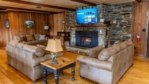 A cozy living room with two leather sofas, a wooden coffee table, and a stone fireplace. - The Valley Lodge Sleeps 12 (Spruce Pine)