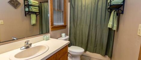 A bathroom with a sink, toilet, and green shower curtain.