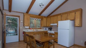 A compact kitchen with wooden cabinets, a white refrigerator, and a dining table with chairs. - The Ridge Cabin - Sleeps 4 (Spruce Pine)