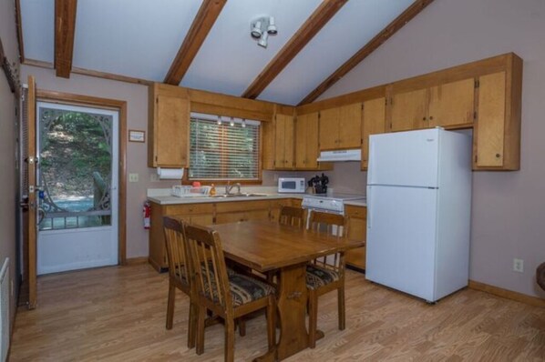 A compact kitchen with wooden cabinets, a white refrigerator, and a dining table with chairs.