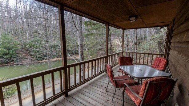 A covered outdoor deck with a table and chairs, overlooking a wooded area and a body of water. - The Ridge Cabin - Sleeps 4 (Spruce Pine)