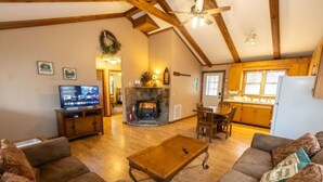A cozy living room with a fireplace, wooden beams, and a television. - The Ridge Cabin - Sleeps 4 (Spruce Pine)