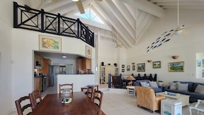 A spacious living area with a high ceiling, a dining table with chairs, a sofa, and a ceiling fan.