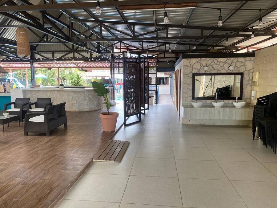 A spacious indoor area with a wooden floor, a seating area with chairs, a potted plant, and a counter with sinks.