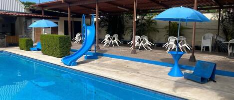 A swimming pool with a slide, lounge chairs, and umbrellas.