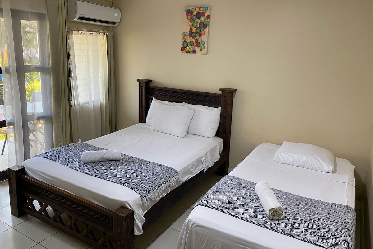 Une chambre d’hôtel avec deux lits, une fenêtre avec des rideaux, un appareil de climatisation et une décoration murale colorée.