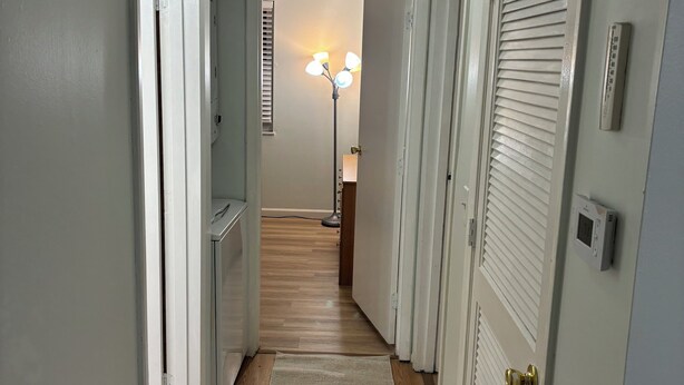 Un couloir aux murs blancs, doté d’un plancher en bois et d’un luminaire au plafond.