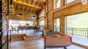A wooden interior with a foosball table, dining area, and large windows. - CHALET DES FEES - BEAUFORT (BEAUFORT)