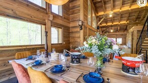 A wooden dining area with a table set for four, featuring blue and white dishes, a vase of flowers, and a red pan on the table. - CHALET DES FEES - BEAUFORT (BEAUFORT)