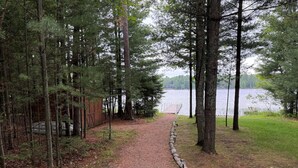 Un sentiero sterrato conduce a un molo di legno lungo un lago, circondato da alberi alti.