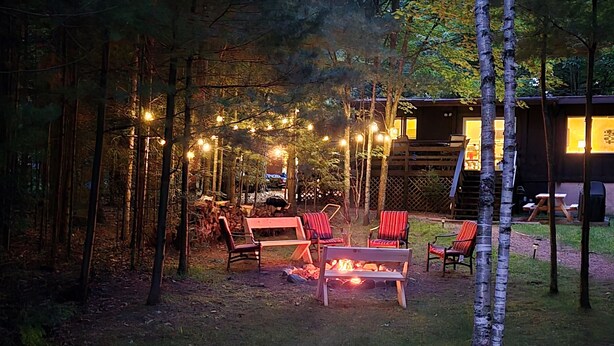 Un'accogliente zona relax all'aperto con un braciere, circondata da alberi e luci decorative.