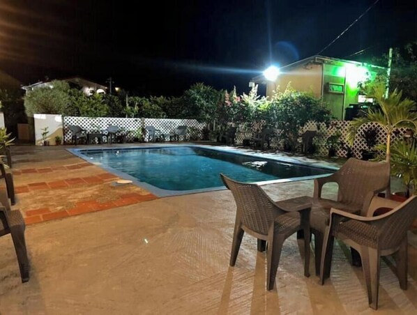 A swimming pool with a tiled deck, surrounded by chairs and potted plants.