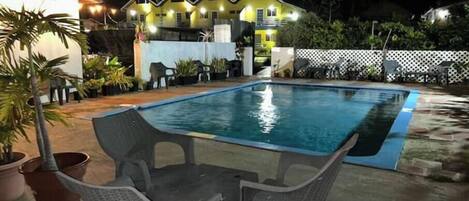 A swimming pool with a small table and chairs in the foreground, surrounded by potted plants and a white fence.