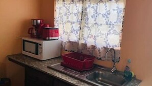Uma cozinha compacta com micro-ondas, uma cesta vermelha, pia e janela com cortinas florais.