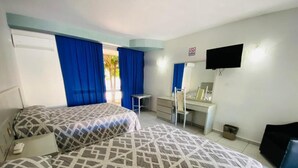 Habitación de hotel con dos camas, un escritorio, una silla, un televisor y una ventana con cortinas.
