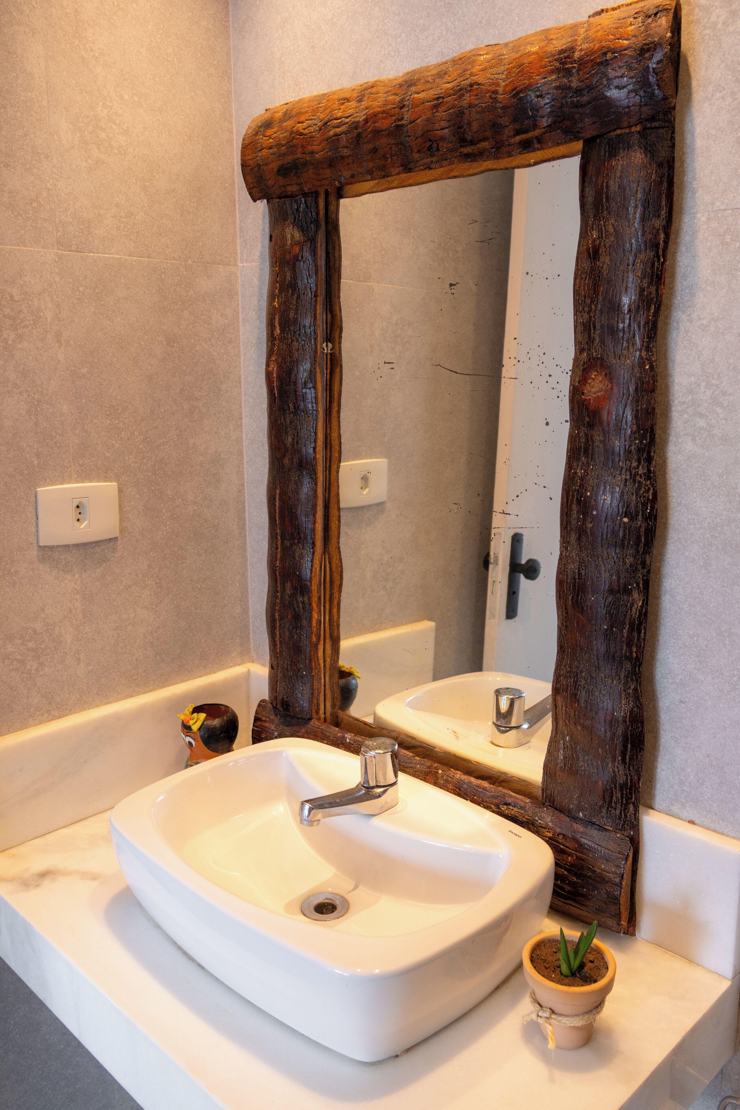 Une salle de bain avec un lavabo blanc, un miroir encadré en bois et une petite plante en pot.
