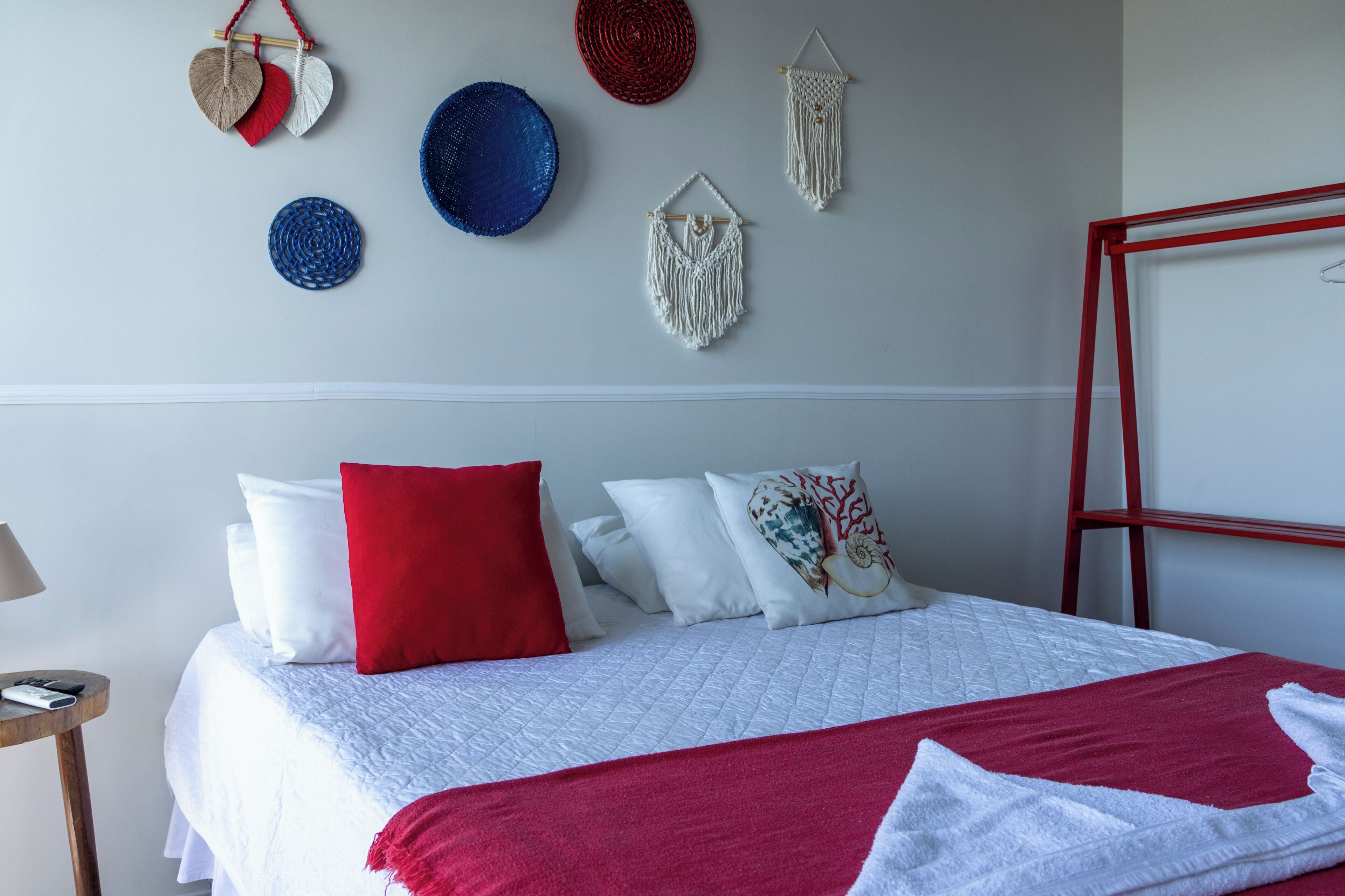 Una cama bien hecha con ropa de cama blanca y roja, una mesita de noche con una lámpara y adornos en la pared.