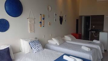 Quarto de hotel com duas camas, um tapete azul e decorações na parede, incluindo um pendente de macramé e objetos de madeira.