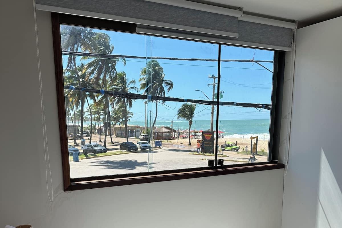 Ein Zimmer mit einem Bett, einem Fenster mit Blick auf den Strand und einem Strandsonnenschirm draußen.