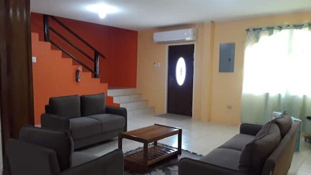 A living room with a sofa set, a coffee table, a staircase, and a door with a light fixture.