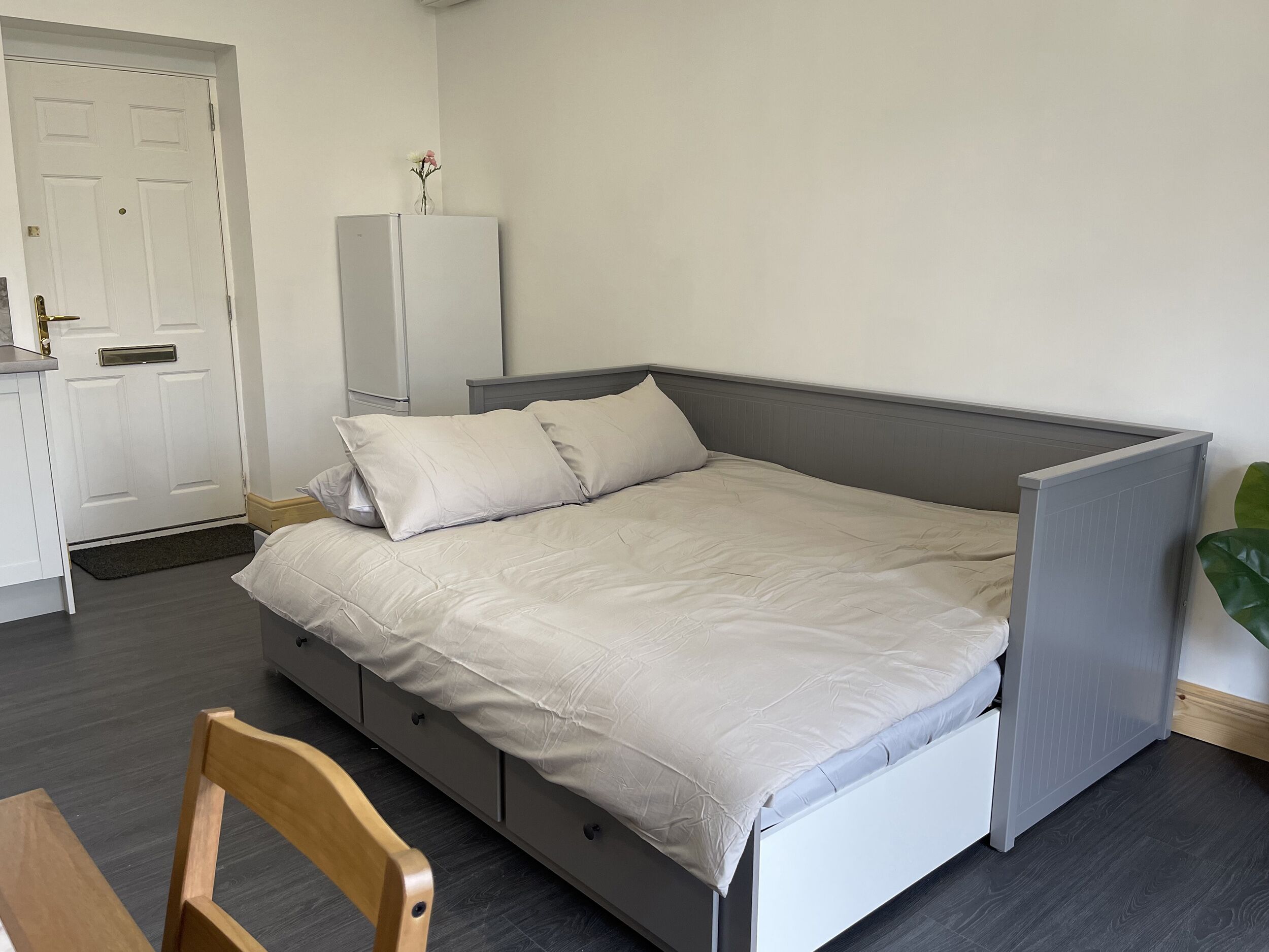Een slaapkamer met een bed, een houten stoel, een witte kledingkast en een deur.
