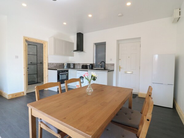 A compact kitchen with a dining area, including a wooden table and chairs, a built-in oven, and a white refrigerator.