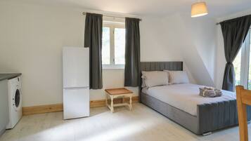 A compact room with a bed, a small table, a washing machine, and a refrigerator.