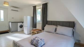 Een compacte slaapkamer met een bed, een klein tafeltje en een kitchenette, inclusief een wasmachine en een koelkast.