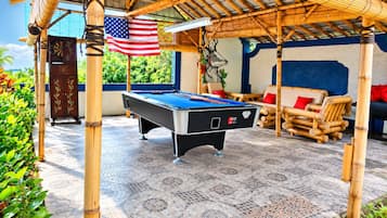 Ein Billardtisch mit einer amerikanischen Flagge, umgeben von Bambusmöbeln und einer blauen Wand mit Wandgemälde.