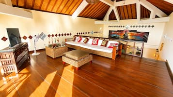 A spacious living area with a high ceiling, a sofa set, a television, and decorative wall art.
