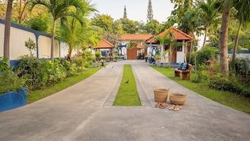 Un chemin menant à un bâtiment doté d’un toit en tuiles, entouré d’une végétation luxuriante et de palmiers.