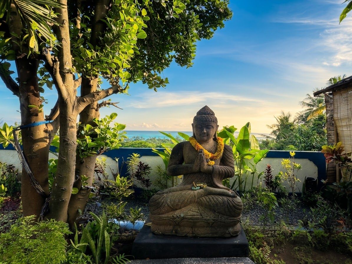 Una estatua sentada en posición meditativa, rodeada de abundante vegetación y un cielo despejado.