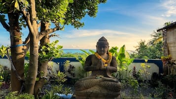 Una estatua sentada en posición meditativa, rodeada de abundante vegetación y un cielo despejado.