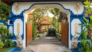 Un portail traditionnel, avec un chemin menant à un bâtiment, le tout entouré d’une végétation luxuriante.