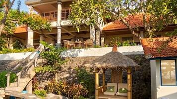 A hotel with a stone staircase leading to a covered area with a thatched roof seating area.