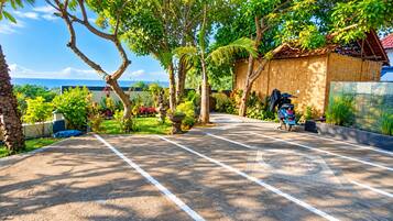 Ein gepflasterter Parkplatz mit einem abgestellten Roller, umgeben von üppiger Vegetation und Blick aufs Meer.