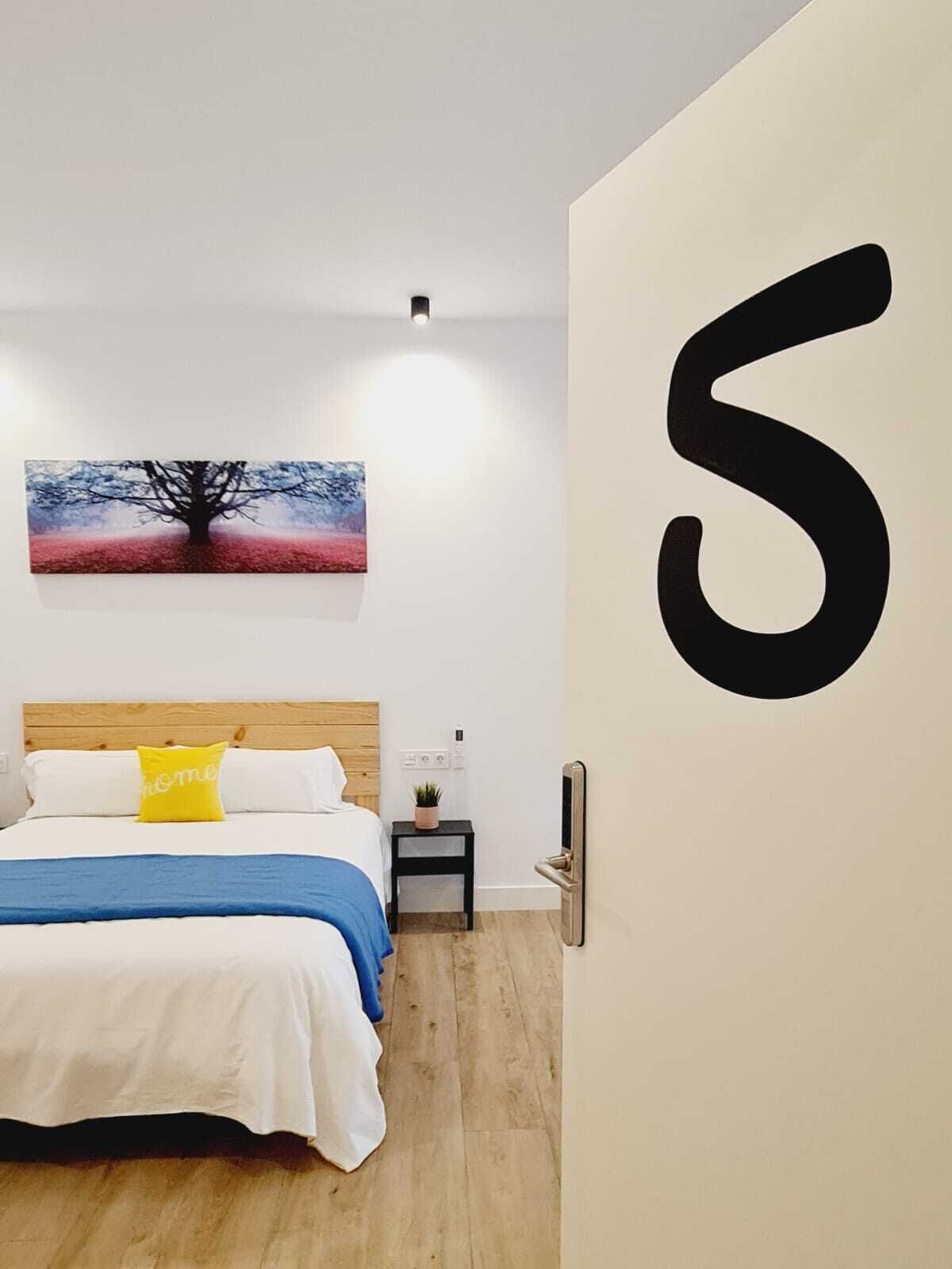 Een slaapkamer met een bed, een nachtkastje, een kunstwerk aan de muur en een groot getal op de muur.