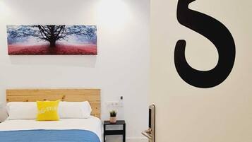 Een slaapkamer met een bed, een nachtkastje, een kunstwerk aan de muur en een groot getal op de muur.